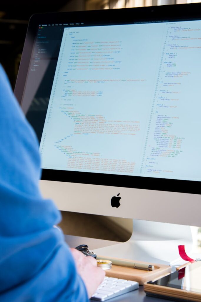 A programmer in a blue shirt coding on an iMac. Perfect for technology or work-related themes.